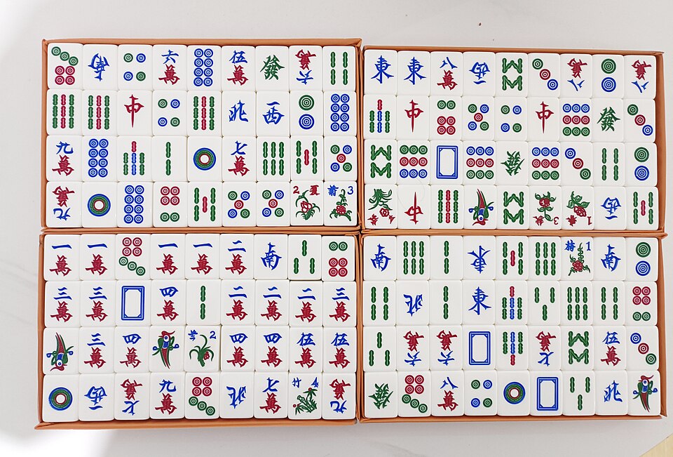 Photograph of a physical Chinese-style Mahjong set showing real bamboo, circle, character, Wind, Dragon, and Flower tiles